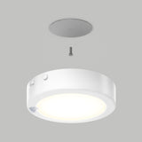 A round, white ceiling light fixture is shown being installed with a single screw and a circular mounting plate on a gray ceiling. The light is illuminated, and the components are aligned vertically.