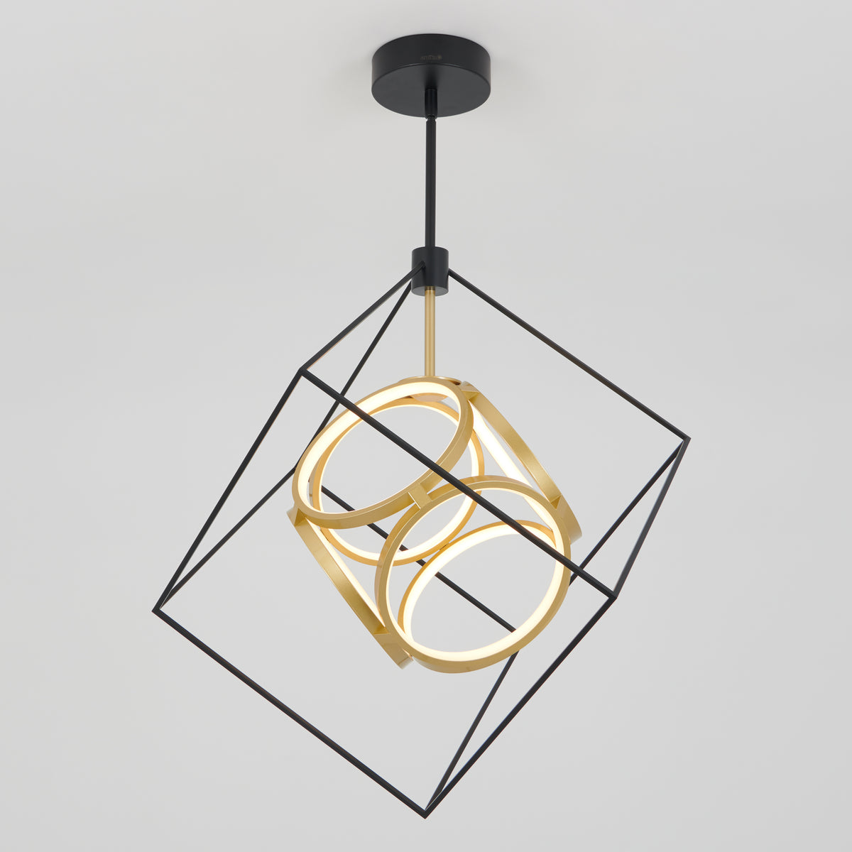 Modern pendant light featuring a black metal cube frame with two gold rings inside, both illuminated, hanging from a black ceiling mount against a plain white background.