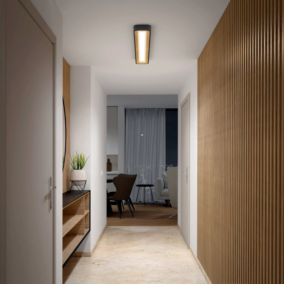 A modern hallway with light wood floors and walls features an Artika Alton 48 in. LED flush mount light (5 CCT) overhead, a wooden console table with plants and a mirror on the left, and a view into a living area with desk, chair, and window.