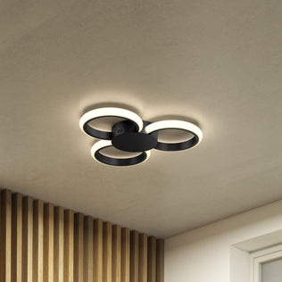 The Artika Nyala 15 in. LED flush mount light 5CCT features three overlapping circular rings on a smooth ceiling, casting a warm glow. Wooden slats and part of a window frame are visible in the room's corner.