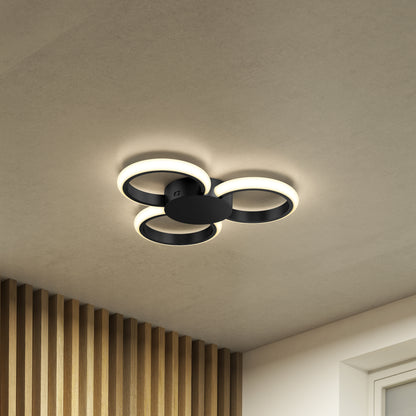 The Artika Nyala 15 in. LED flush mount light 5CCT features three overlapping circular rings on a smooth ceiling, casting a warm glow. Wooden slats and part of a window frame are visible in the room's corner.