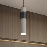 A modern cylindrical pendant light with a concrete finish and black accent hangs from the ceiling in front of wooden cabinets with subtle lighting below.