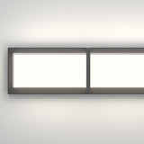 A modern rectangular wall light fixture with a black frame and a dividing vertical strip, mounted on a white wall and casting a soft glow.