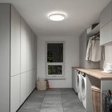 A modern laundry room with light gray cabinets, a wooden countertop, a washer and dryer, hanging clothes, a window with greenery outside, and laundry baskets on the floor. The room is well-lit by a ceiling light.