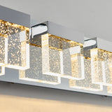 Close-up of a modern wall light fixture with rectangular glass shades containing small bubbles, mounted on a shiny chrome base and emitting a warm, glowing light.