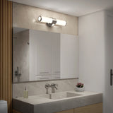 A modern bathroom with a large mirror above a double sink, a wall-mounted faucet, a soap dispenser, a bowl of small flowers, and a sleek horizontal light fixture above the mirror.