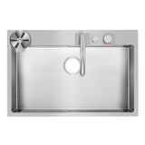 Top-down view of a modern stainless steel kitchen sink with a single basin, a circular drain, a curved faucet, and two control knobs on the right side. A removable drain strainer is on the upper left corner.