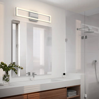 Modern bathroom featuring a large mirror with the Artika Dover 27-in Integrated LED 5-CCT Vanity Light Bar above, double sinks with chrome minimalistic faucets, a wooden vanity, green plant, and glass shower with rainfall showerhead.