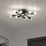 A modern ceiling light fixture with a black metal frame and six exposed round bulbs, arranged in a geometric, intersecting pattern, illuminating a white ceiling in a contemporary room.