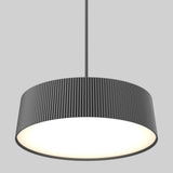 A modern, circular pendant light with a ribbed, dark gray lampshade hangs from the ceiling, emitting a soft, bright white light against a plain gray background.