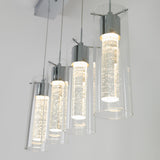 Four modern pendant lights with cylindrical glass shades and metallic fixtures hang in a row from the ceiling, each containing illuminated, bubble-filled rods, creating a contemporary and stylish look.