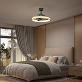 A modern bedroom with a large bed, gray and beige bedding, a wooden nightstand, floor-length curtains, and a contemporary ceiling fan with a ring light overhead. Soft daylight enters through a window.