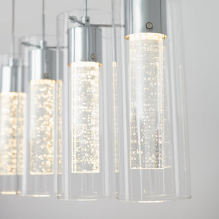 Close-up of the Artika Essence 4-light LED pendant, showcasing cylindrical clear glass with chrome accents and bubble-filled inner tubes, emitting a bright white glow against a plain background.