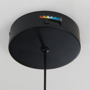 A close-up of the Artika Raina LED pendant light 5 CCT, a round black ceiling fixture with a hanging cord and a small side label featuring color-coded triangles and numbers.
