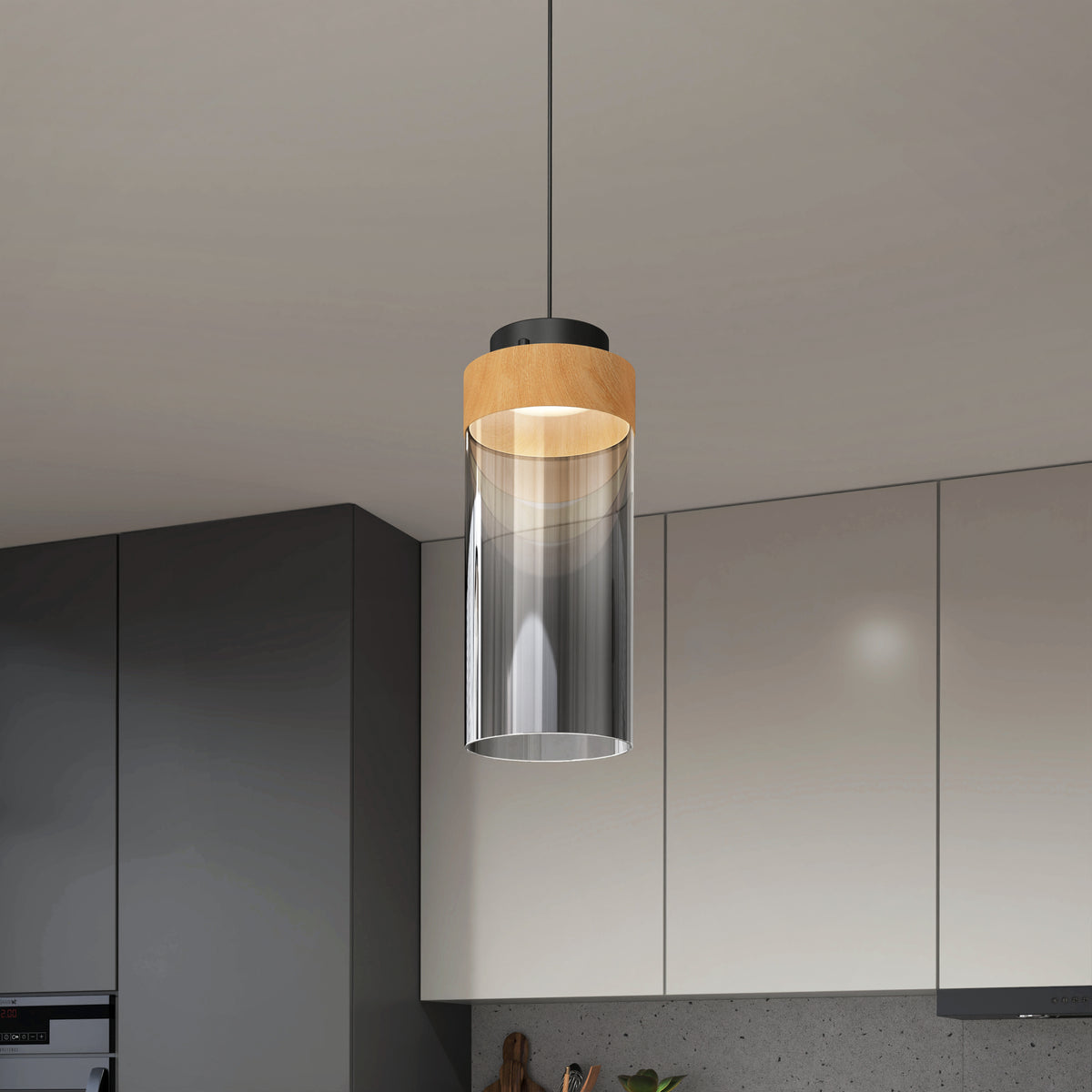 A modern pendant light with a cylindrical clear glass shade and a wooden accent hangs from the ceiling in a contemporary kitchen with gray and white cabinets.