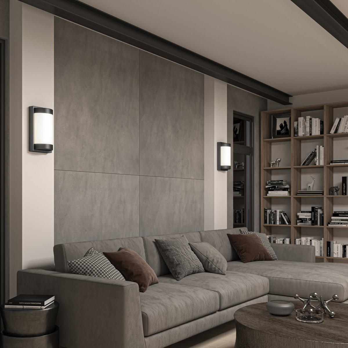 A modern living room featuring a gray sectional sofa with assorted cushions, a round coffee table, built-in bookshelves filled with books, and two wall-mounted lights on a textured gray accent wall.