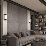 A modern living room featuring a gray sectional sofa with assorted cushions, a round coffee table, built-in bookshelves filled with books, and two wall-mounted lights on a textured gray accent wall.