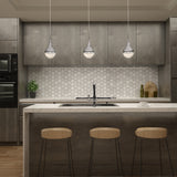 Modern kitchen with dark wood cabinets, a white hexagon tile backsplash, an island with a marble countertop, three wooden bar stools, three pendant lights, and decorative plants and dishes on the counter.