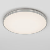 A round, modern ceiling light fixture with a white frosted cover and a slim metallic rim, mounted on a plain white ceiling, emitting a soft, even glow.