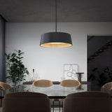 A modern dining room with a glass table, beige chairs, a large black pendant light, a potted plant, abstract artwork, and a staircase in the background. The room has minimalist decor and neutral colors.
