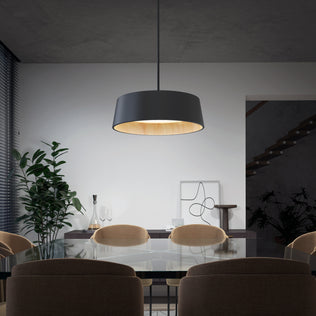 A modern dining room featuring a glass table, beige chairs, Artikas Alton modern LED pendant light 5 CCT, indoor plants, minimalist artwork, a staircase in the background, and natural light filtering through window blinds on the left.
