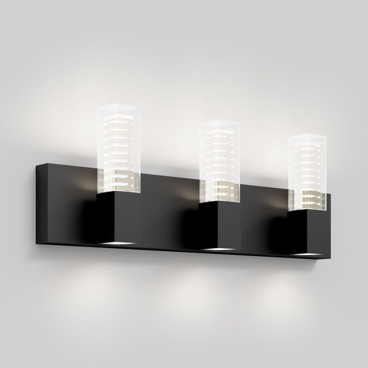 A modern wall sconce light fixture with three square black bases, each holding a clear rectangular glass shade, mounted on a matching black horizontal bar against a light grey wall.