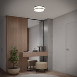 A modern entryway features a wooden accent wall, a tall mirror, a floating wooden console with decorative items, a potted plant, two round ottomans, and a ceiling light fixture.