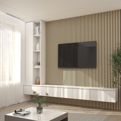 Modern living room with a mounted flat-screen TV on an Artika Sonolok sound-absorbing wall panel kit, floating white shelf, large window with sheer curtains, potted plant, and white coffee table with vase and magazines.