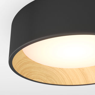Close-up of the Artika Alton LED flush mount, showcasing its black outer rim, wooden inner ring, and bright white center glow—an elegant example of modern ceiling lighting.