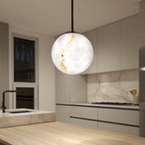 A modern kitchen with beige cabinets and marble countertops features a large, glowing spherical pendant light with white and gold veining hanging above a wooden island. A window shows a nighttime outdoor scene.