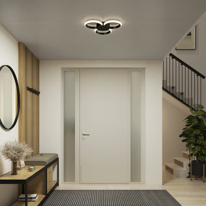 Modern entryway with a white front door, frosted glass side panels, black bench holding dried flowers, round mirror, wall hooks, plant, and staircase with black railing. Lit by the Artika Nyala 15 in. LED flush mount light 5CCT overhead.