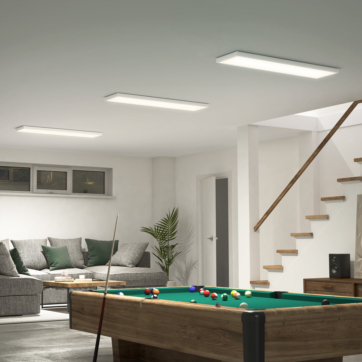 A modern basement features a pool table, gray sectional, green pillows, a plant, wooden stairs, and Artika Skyshade RGB LED panels.