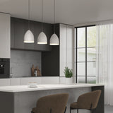A modern kitchen with pendant lights over a white island, two brown chairs, a cup and saucer, a plant pot, and large windows with sheer curtains letting in natural light.