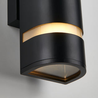 A close-up of the Artika D4 indoor-outdoor wall light, a modern black cylindrical sconce with a horizontal frosted strip near the top that glows warmly, shown mounted on a light-colored wall.
