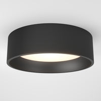 The Artika Alton LED flush mount is a modern circular black ceiling light installed on a white ceiling, emitting a soft white glow from its center.