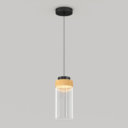 The Artika Hanson 1-light LED pendant 5 CCT features a black ceiling mount, black cord, wooden accent, and clear cylindrical glass shade, shown against a plain light gray background.