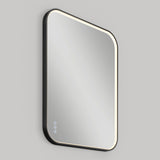 A modern, rectangular mirror with rounded corners, a black frame, and built-in LED lighting around the edges. Three touch-sensitive control icons are visible in the lower left corner. The mirror is mounted on a gray wall.