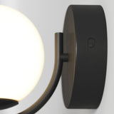 A close-up of a modern wall-mounted light fixture with a round, frosted glass shade and a dark, circular metal base featuring a small push button.