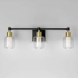 A modern wall-mounted light fixture with three cylindrical glass shades, each containing a textured inner cylinder. The fixture features black and gold accents against a plain light gray background.
