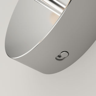 Close-up of the Artika DNA modern LED wall sconce 3 CCT, a sleek metallic fixture with a small round button and integrated LED light. Its polished surface reflects light, emphasizing its contemporary design against a plain background.