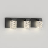A modern wall-mounted light fixture with three square crystal glass shades, each emitting a bright white light, set on a rectangular black metal base against a plain light gray wall.