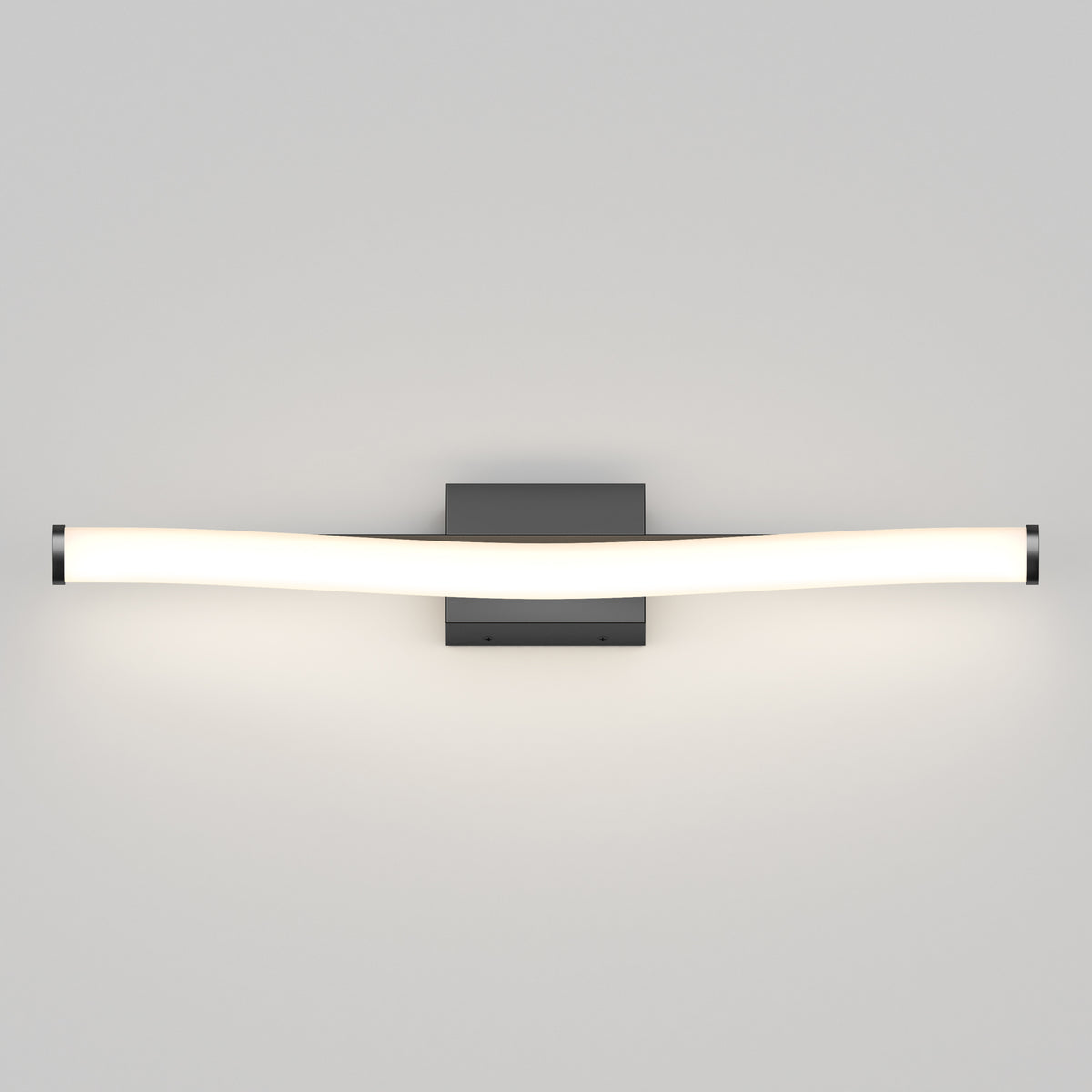 A modern wall-mounted light fixture with a gently curved, elongated frosted tube attached to a rectangular black base, emitting a soft white glow against a light gray wall.