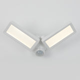 A white, modern LED security light fixture with two rectangular panels angled outward and a motion sensor centered below them, mounted on a plain, light gray background.