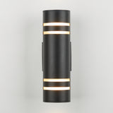 A modern cylindrical black wall sconce light fixture with horizontal frosted strips emits a soft white glow through openings near the top and bottom, set against a plain light gray background.
