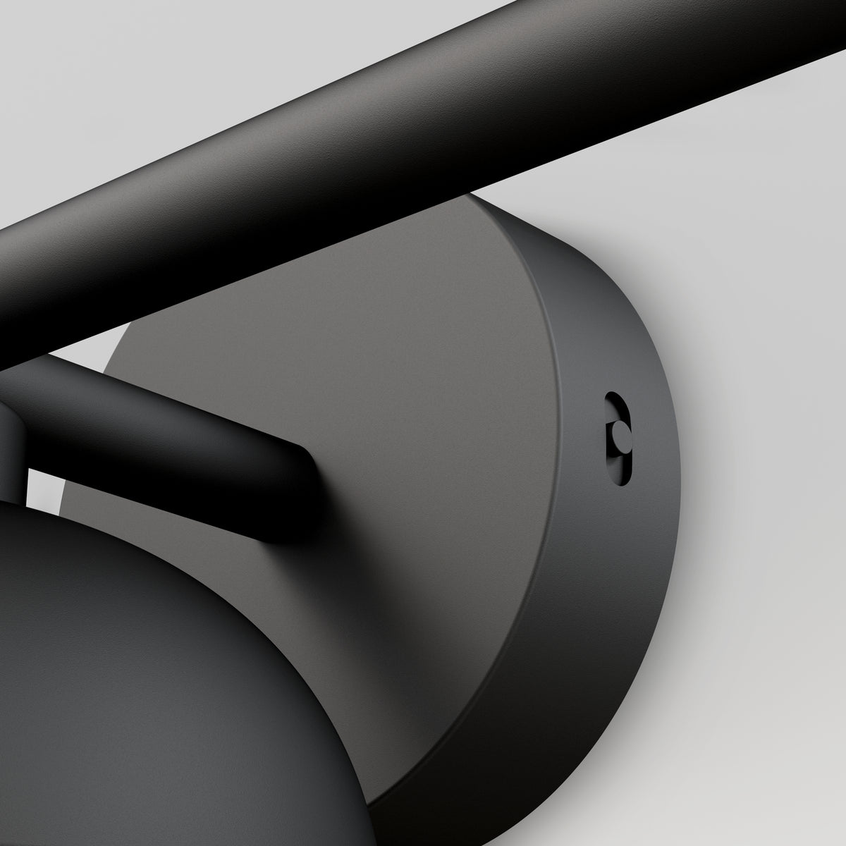 Close-up view of a matte black cylindrical wall mount with a horizontal rod and a round base, set against a light gray background. The image emphasizes the modern, minimalist design and smooth finish.
