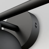 Close-up view of a matte black cylindrical wall mount with a horizontal rod and a round base, set against a light gray background. The image emphasizes the modern, minimalist design and smooth finish.