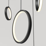 Close-up of three modern, circular pendant lights with black frames and glowing white interiors, suspended by thin cables against a plain, light gray background.