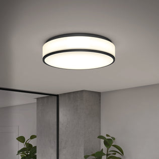 The Artika Giada 15 in. LED modern flush mount light with black trim is installed on a white ceiling in a minimalist room featuring a gray concrete pillar, large mirror, and green potted plants.