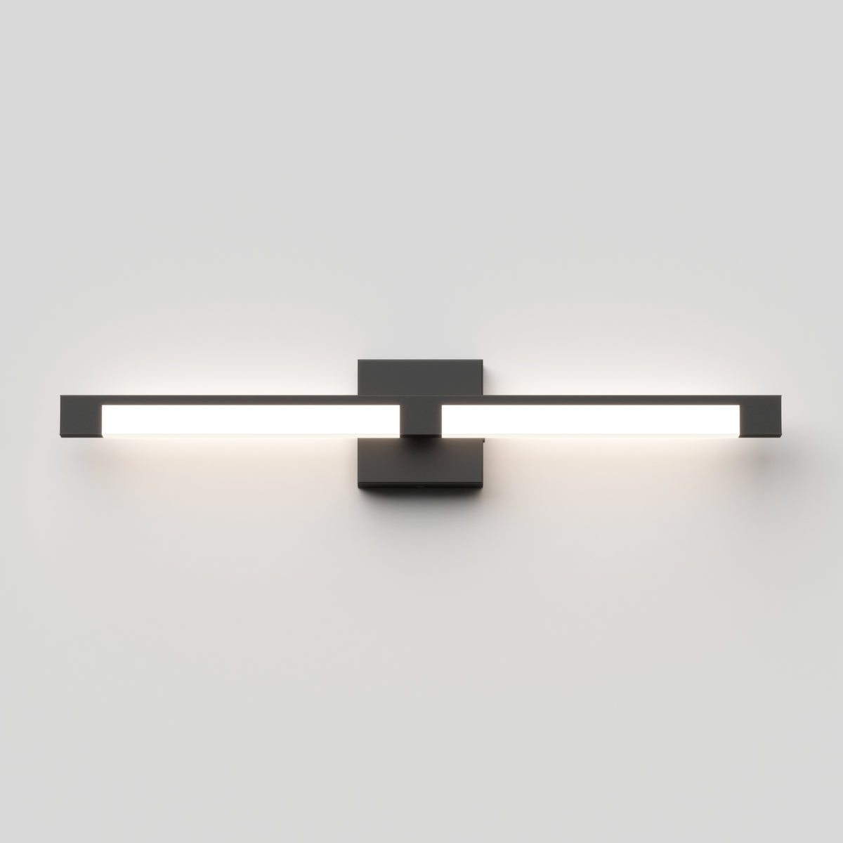A modern, wall-mounted LED light fixture with a minimalist black rectangular base and two horizontal light bars extending outwards, emitting a bright white glow against a plain, light gray wall.