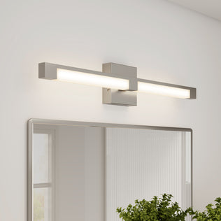 The Artika Tivoli modern LED bathroom vanity light 5 CCT, with a rectangular metal base and dimmable LED, is wall-mounted above the mirror. A green plant sits partially visible on the countertop below.